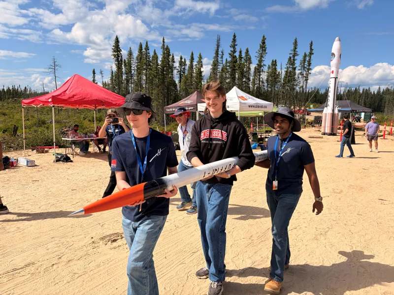 Three team members carrying Puffin-1 at the launch site