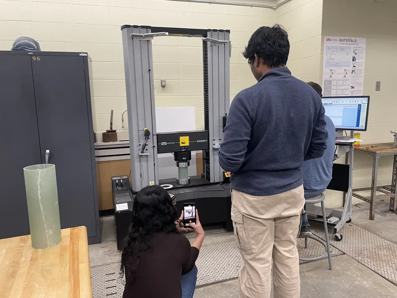 Team members at an Instron test machine with a tube specimen