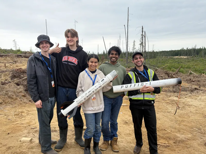 Team members holding recovered rocket sections in a clearing