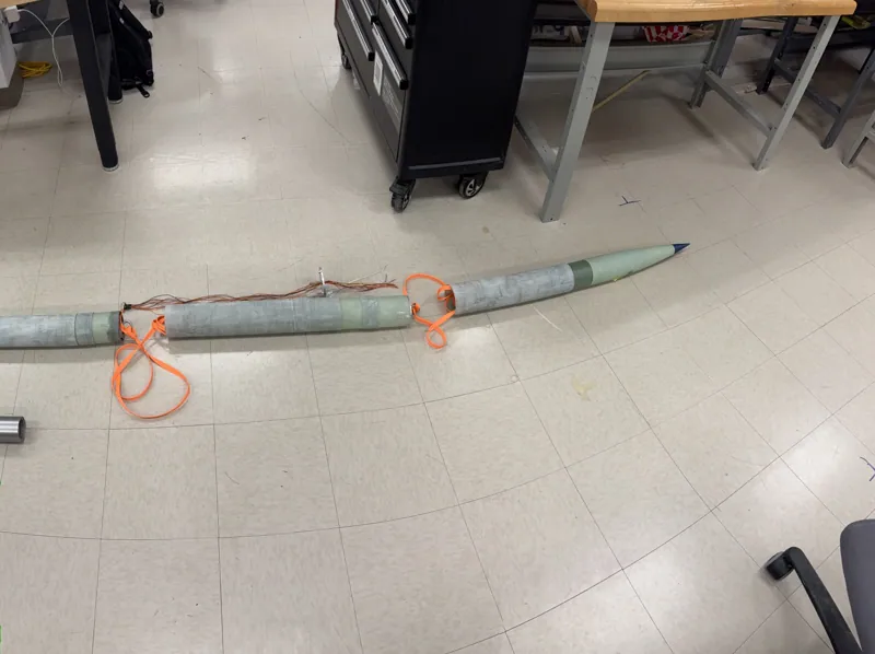 Unpainted rocket sections, fins and recovery harness during workshop assembly